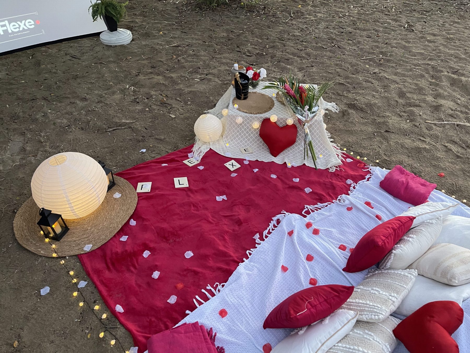 Plaid rouge, lanternes et pétales sur le sable, prêt pour la séance
